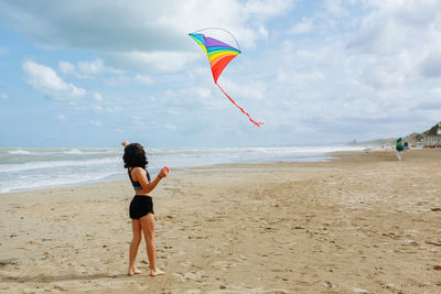 Rear view of woman doing yoga at beach against sky