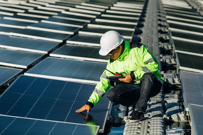 Male electrician in white safety helmet standing  and mounting photovoltaic solar panel