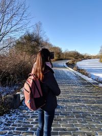 Rear view of woman standing on a riverside footpath against sky