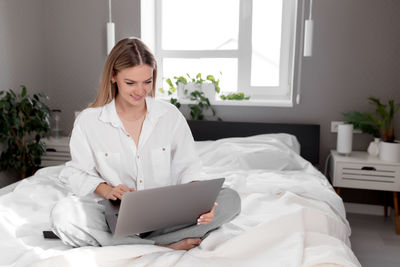 Mid adult woman using mobile phone while sitting on bed