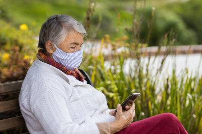 Senior woman wearing mask using smart phone outdoors