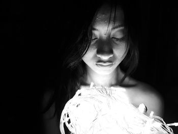 Woman holding illuminated string light over black background