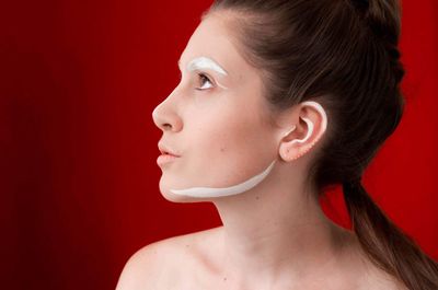 Close-up of young woman with face paint against red background