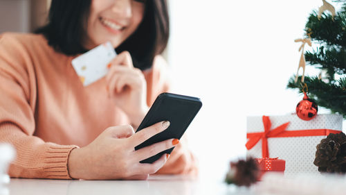 Midsection of woman holding credit card while using phone on table