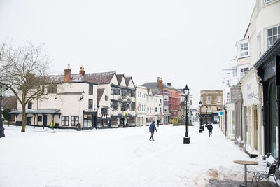 Man walking on snow covered city against clear sky