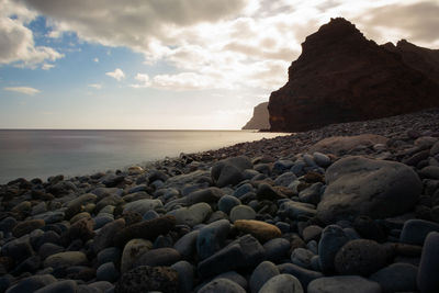 Rocks on beach against sky during sunset