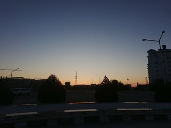 Silhouette of city street against clear sky at sunset