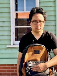 Portrait of young asian man in eyeglasses sitting on the sidewalk against building exterior.