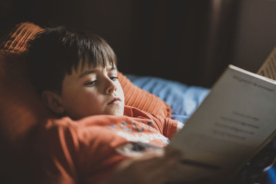 Boy reading book while lying on bed at home