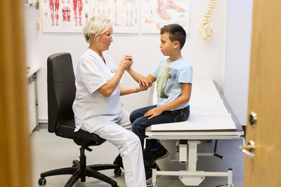 Senior female orthopedist examining boy's hand at clinic