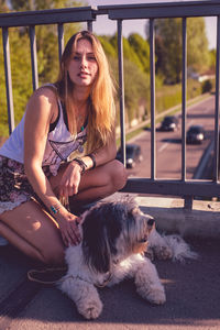 Portrait of young woman with dog sitting by railing on footbridge