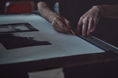 Midsection of man drawing in paper at darkroom