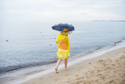 Woman with umbrella walking at sea shore