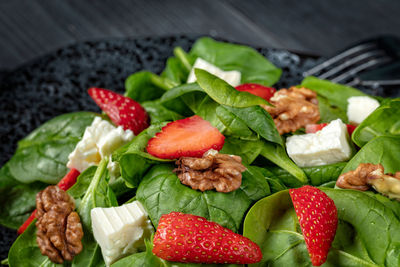 Strawberry spinach salad with feta cheese, walnuts, olive oil, on black plate, on dark background