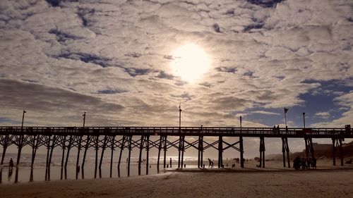 Pier on beach against cloudy sky during sunset