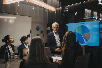 Senior businessman discussing plans with male and female colleagues in board room