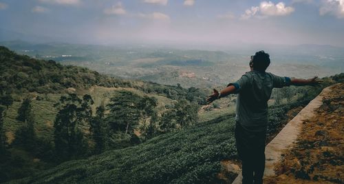 Rear view of man standing on mountain against sky