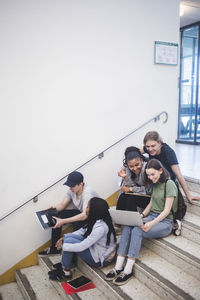 Full length of happy multi-ethnic students talking and sitting on steps at high school