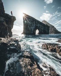 Low angle view of man standing on cliff by sea against sky