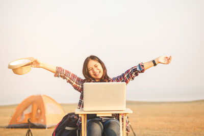 Smiling young woman sitting on the land against sky