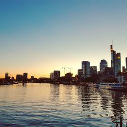 River by city buildings against sky during sunset