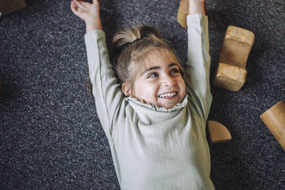 Directly above view of happy girl lying down with arms raised in classroom