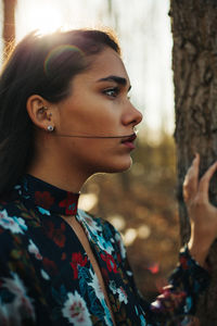 Close-up of thoughtful beautiful woman looking away while standing by tree trunk