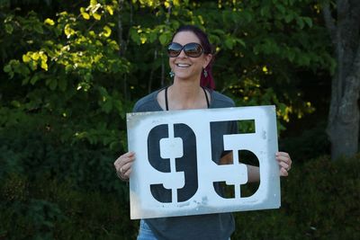 Smiling woman wearing sunglasses while holding numbers on board at park