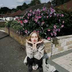 Woman puckering lips while crouching against flowering plants in city