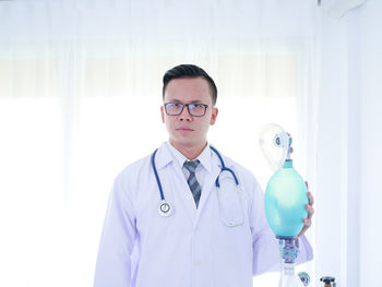 Portrait of doctor wearing eyeglasses while holding oxygen mask at hospital