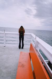 Rear view of woman standing on pier over sea against sky