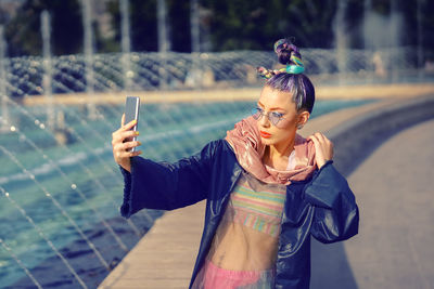 Young funky fashion woman with trendy look taking selfie outdoors