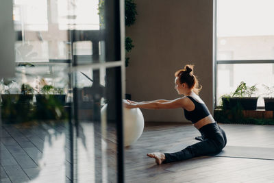 Full length of woman sitting on floor by window