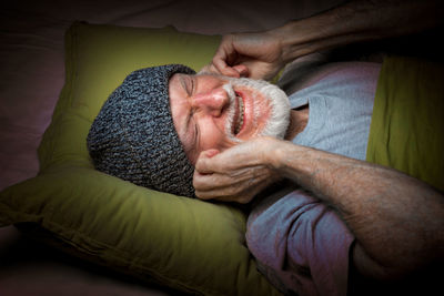 Senior man covering ears on bed at home