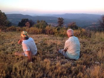 Couple of older brothers from the back, sitting on the ground looking at the landscape in the sunset