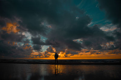 Silhouette man standing at beach against cloudy sky during sunset