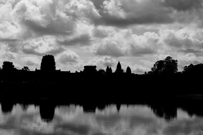 Silhouette trees by river against sky