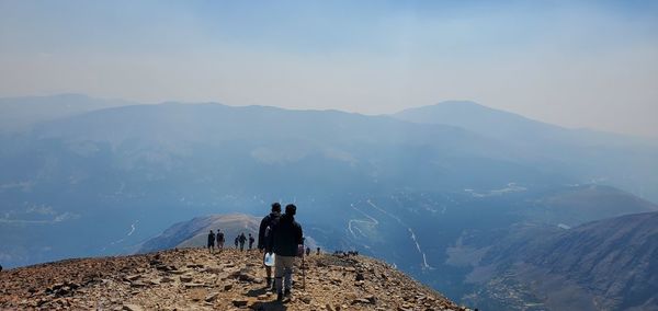 Rear view of people standing on mountain against sky