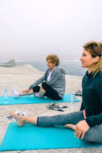 Female friends doing yoga by sea on walkway