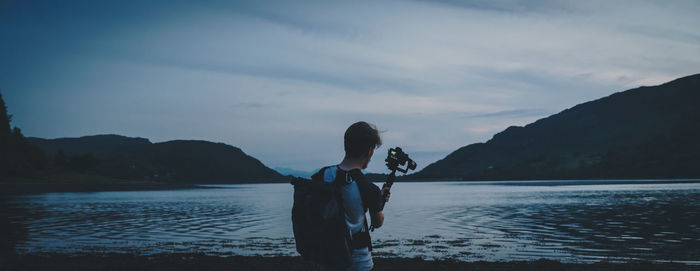 Rear view of young man standing by lake