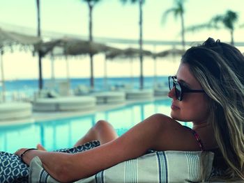 Young woman wearing sunglasses while relaxing by swimming pool