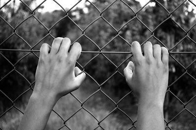 Close-up of human hand on chainlink fence