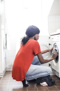 Full length side view of mid adult woman putting clothes into washing machine at home