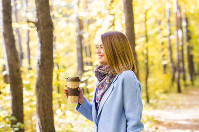Young woman standing by tree in forest during autumn