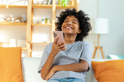 Young woman using mobile phone while sitting on bed at home
