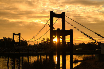 Silhouette bridge over river against sky during sunset