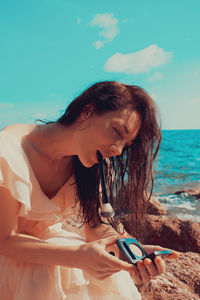 Woman holding beauty products and brush at beach against sky