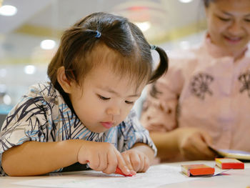 Cute baby girl coloring paper at table in restaurant