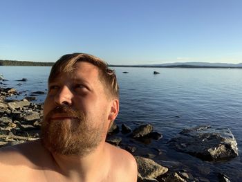 Portrait of man on rock at beach against clear sky