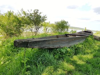 Abandoned boat on grassy field against sky